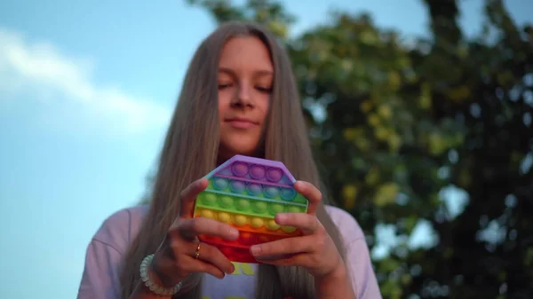 En flicka med långt hår spelar popit i naturen. Pop det är en populär silikonleksak för barn. — Stockfoto