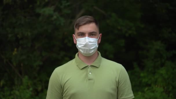 De jongeman doet zijn medisch masker af en gooit het weg. Een man in de natuur met een masker. — Stockvideo