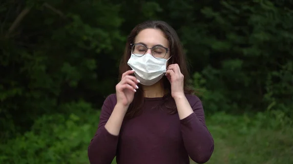 Egy szemüveges fiatal nő leveszi az orvosi maszkot és eldobja. Lány a természetben maszkban. — Stock Fotó