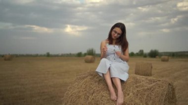 Genç bir kadın samanlıkta oturuyor. Gözlüklü ve mavi elbiseli bir kız..