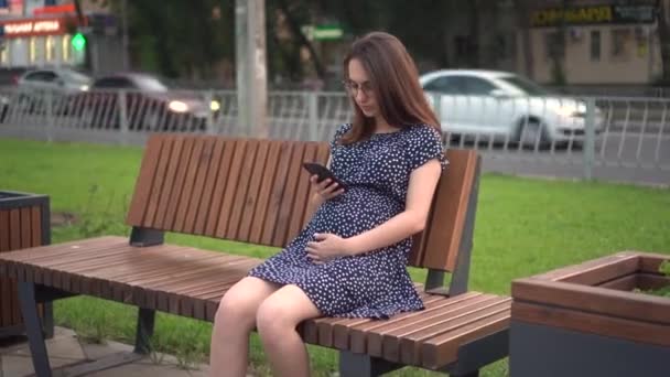 손에 전화기를 쥐고 있는 임신 한 소녀. 안경을 쓰고 드레스를 입은 여자가 전화로 문자를 보내고 있다. — 비디오
