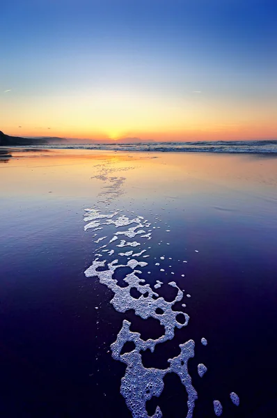 Beach at sunset with foam track — Stock Photo, Image