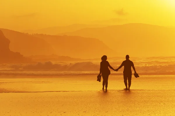 Paar spaziert bei Sonnenuntergang am Strand — Stockfoto