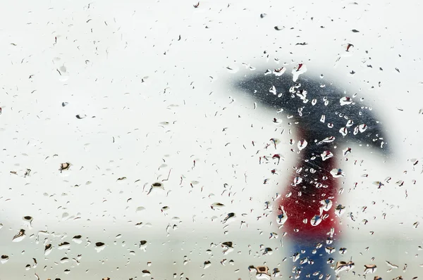 Gotas de lluvia en la ventana con persona con paraguas — Foto de Stock