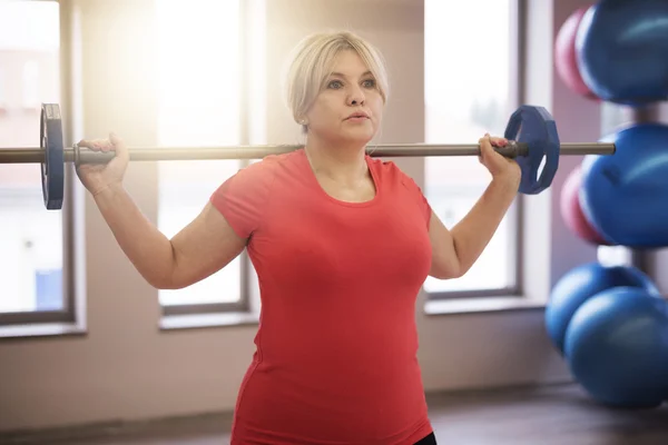 Mulher madura usando barbell no ginásio — Fotografia de Stock