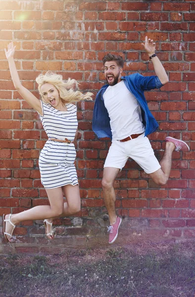 Couple sautant dans l'air devant un mur de briques — Photo
