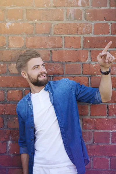 Bonito homem mostrando na parede de tijolo — Fotografia de Stock