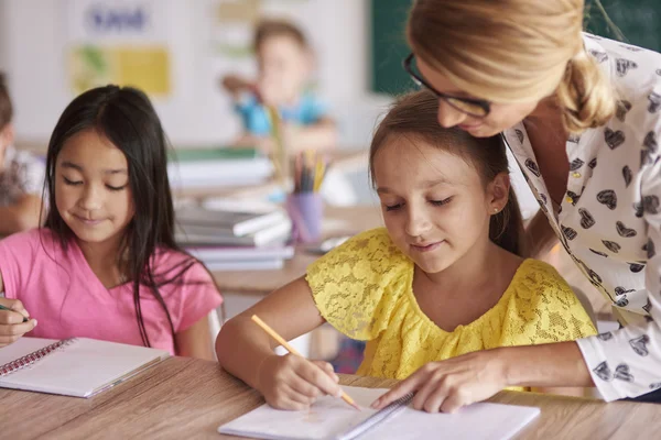 Female teacher helping kids in exercises — Stock Photo, Image