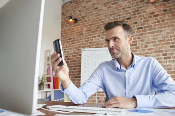 Hombre con teléfono delante de la computadora — Foto de Stock