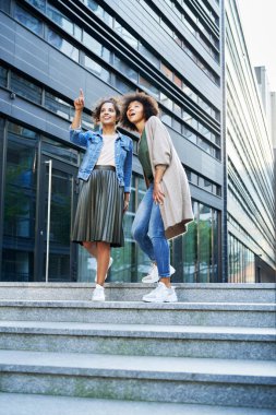 Şehirde yürüyen ve bir şeyi işaret eden iki arkadaş.                               