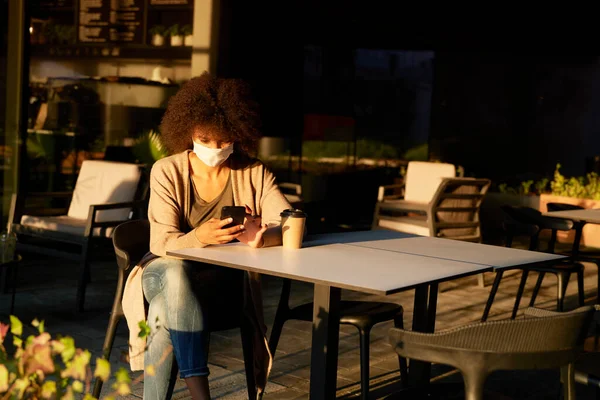 Woman in face mask sitting alone in a cafe