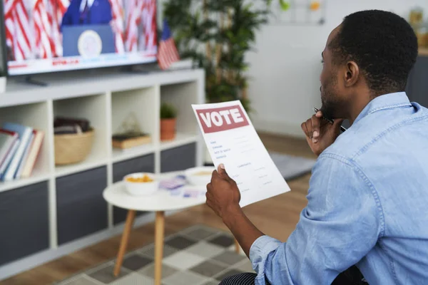Czarny Człowiek Ogląda Telewizję Trzyma Dokument Głosowania — Zdjęcie stockowe