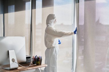 Koruyucu iş kıyafetli biri pencereden dışarı bakıyor.                               