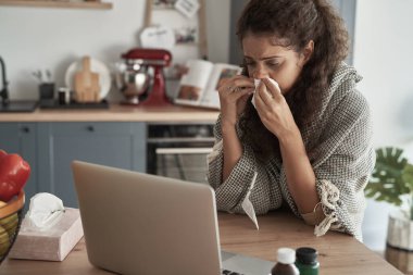 Battaniyeyle kaplı bir dizüstü bilgisayarla oturan hasta kadın.                               