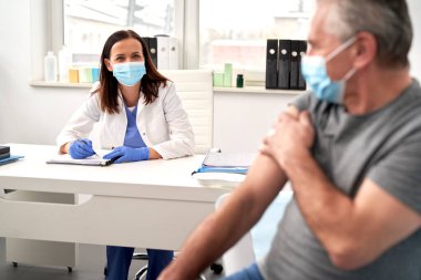 Female doctor talking to senior after vaccination                                clipart