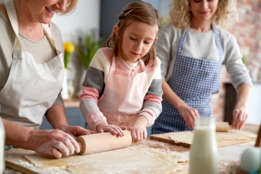 Paskalya kurabiyeleri için hamuru yuvarlayan üç kuşak kadın.                               