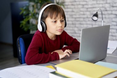 Evde ders çalışırken kulaklık takan konsantre bir çocuk.                               
