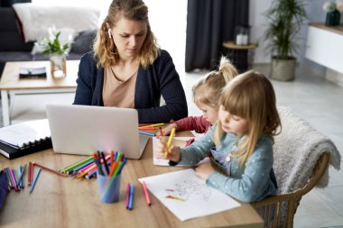 Evde kızlarıyla çalışan meşgul bir anne.                          