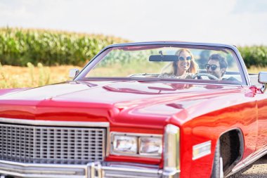 Kırmızı eski bir arabada gülümseyen bir çift.                               