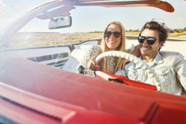 Gülümseyen çift üstü açık arabada özgürce araba sürüyor.                               