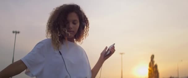 ヘッドフォンでアフリカの若い女性のビデオは 音楽に踊ります 8Kでレッドヘリウムカメラで撮影 — ストック動画