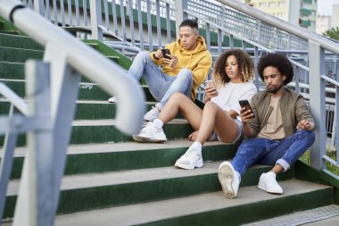 Merdivenlerde cep telefonuyla oturan üç genç.                               