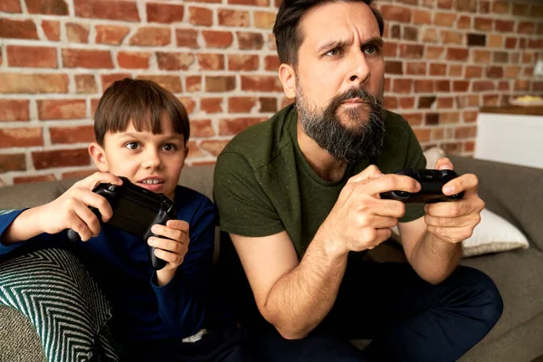 集中的な父と息子が一緒に座ってビデオゲームをプレイ — ストック写真