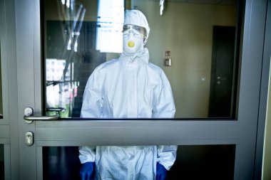 Tehlikeli madde giysisi giymiş biri kapının önünde dezenfekte ediyor.
