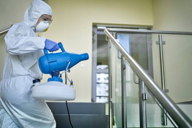 Koruyucu kıyafetli bir kadın merdivenleri dezenfekte ediyor.                               