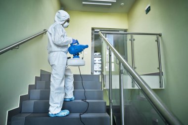 Person in a protective suit disinfecting the staircase clipart