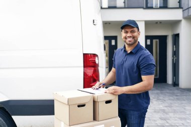 Bir kuryenin portresi bir teslimat aracının yanında paketler ile ayakta duruyor.