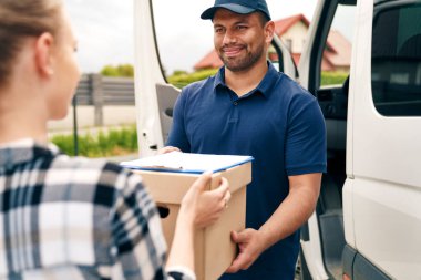 Gülümseyen teslimatçı kadına paket veriyor.