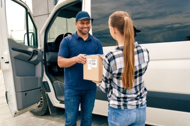 Gülümseyen kurye bir kadına bir paket veriyor.                               