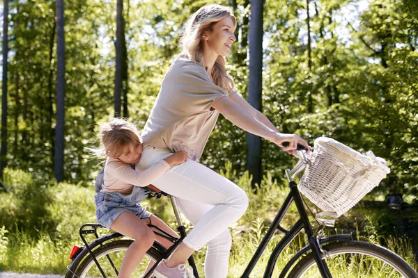 森の中で自転車に乗っている笑顔の母親と娘 — ストック写真