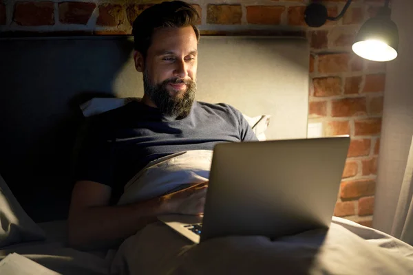 微笑的男人躺在床上 用笔记本电脑 — 图库照片