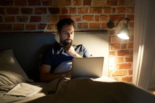 ベッドに横になってノートパソコンを使う男 — ストック写真