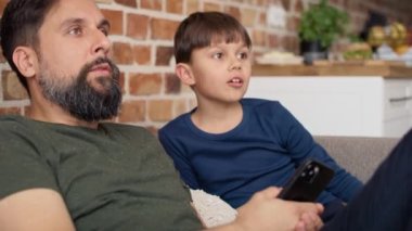 Baba ve oğlunun evde televizyon izlediği videoyu kapat. 8K 'da kırmızı helyum kamerayla çekildi..