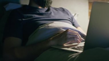 Yatakta yatan ve çalışan bir adamın videosunu kaldır. 8K 'da kırmızı helyum kamerayla çekildi..