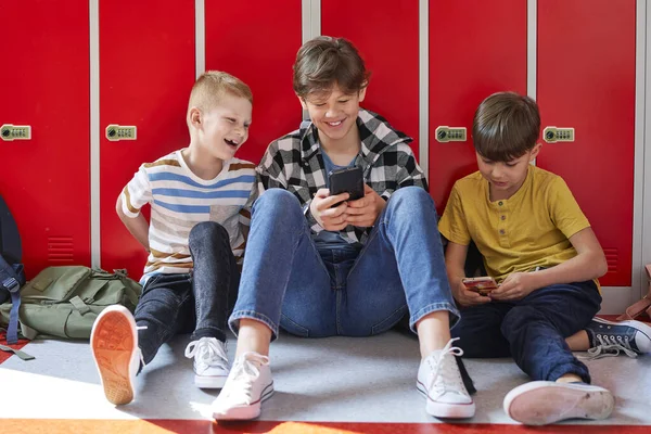 Amigos Sonrientes Sentados Usando Teléfono Inteligente Pasillo Escuela — Foto de Stock