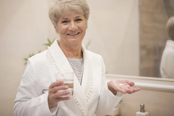 Starsza kobieta z szklanką wody i tabletki — Zdjęcie stockowe
