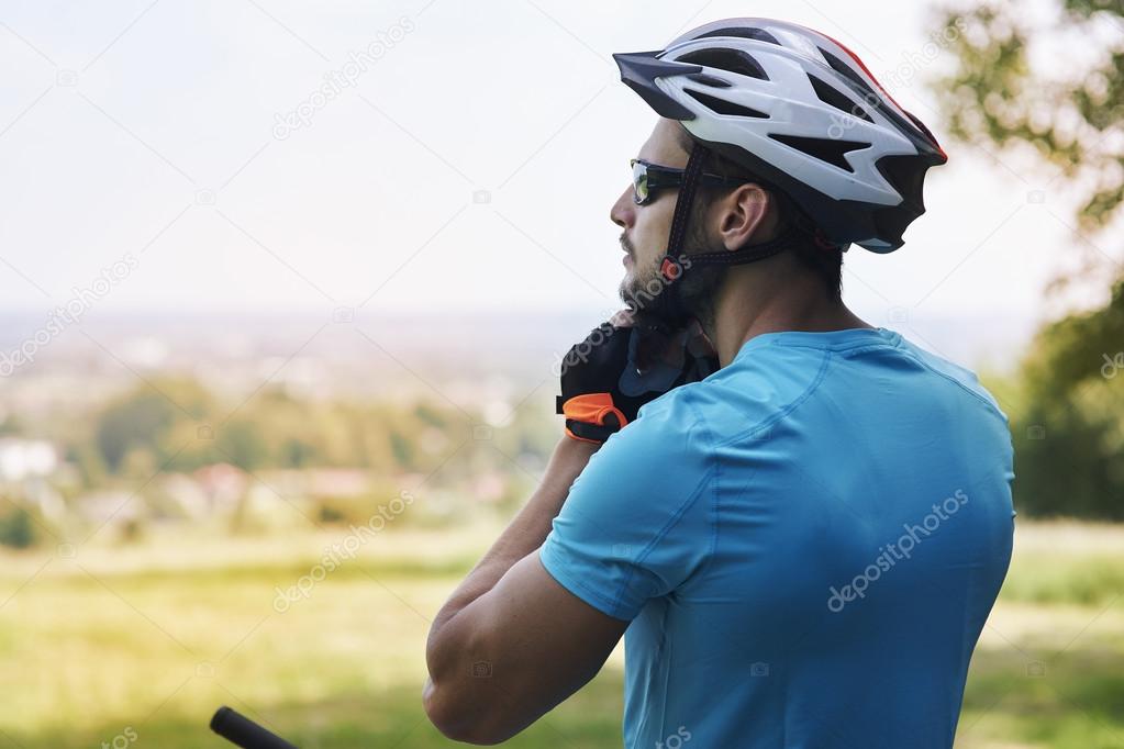 Young man on bicycle touching helmet