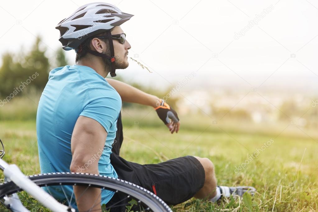 Young man with bicycle  sitting on grass