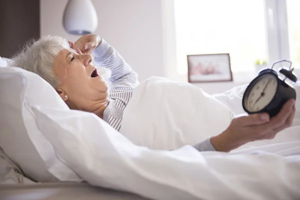 Зрелая женщина в постели с часами — стоковое фото