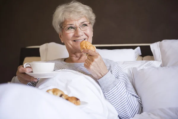 Mujer madura en la cama con comida —  Fotos de Stock