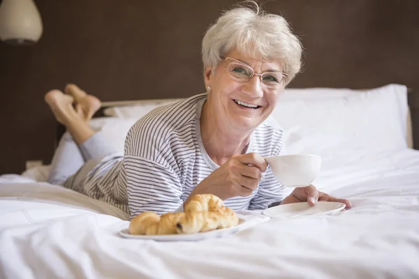 Mature woman in bed with food — Stock Photo, Image