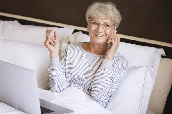 Mature woman talking on mobile phone in bed — Stock Photo, Image