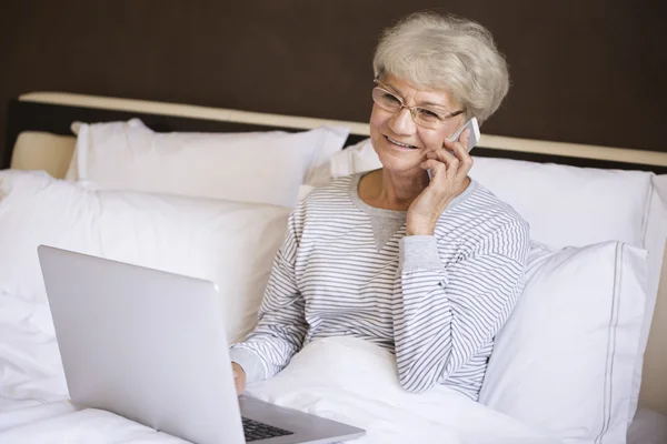 Зрелая женщина разговаривает по мобильному телефону в постели — стоковое фото