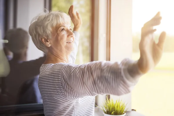 Mujer madura sonriendo cerca de la ventana — Foto de Stock