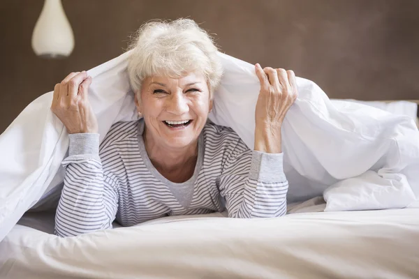 Reife Frau lächelt im Bett — Stockfoto