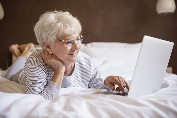 Donna matura con computer portatile a letto — Foto Stock